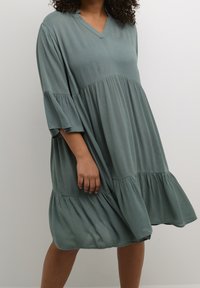 Mint green, knee-length dress with a relaxed fit, V-neckline, and flared 3/4 sleeves. Features a gathered tiered design and lightweight fabric.