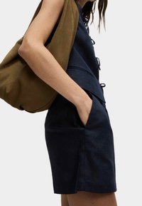 Granatowa bluzka z mieszanki lnu z koronkowymi detalami z przodu, w połączeniu z granatowymi szortami z bocznymi kieszeniami, uzupełniona brązową torebką na ramię.