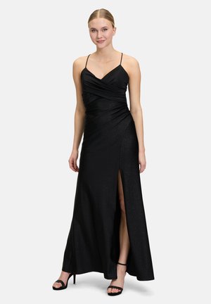 Schwarz Abendkleid mit dünnen Trägern, gerafftem Oberteil, seitlichem Schlitz und schimmernder Stoffstruktur. Kombiniert mit schwarzen Riemchenschuhen.
