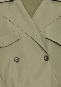 Trench coat verde oliva chiaro con design doppiopetto, ampi revers, due tasche sul petto e bottoni scuri a contrasto.