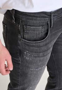 Crne traperice od denima slim kroja, s izbljedenim detaljima, standardnom prednjom džepom i označenom stražnjom etiketom.