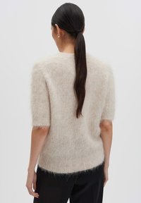 Pull léger beige, à manches courtes, fabriqué dans un matériau doux et pelucheux avec une coupe décontractée. Présente un col rond et des poignets côtelés.