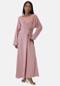 Lang, pink kjole lavet af blødt, tekstureret stof; har bred halsudskæring, lange ærmer, bindebånd i taljen og en sideslids.