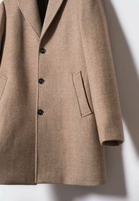 Brązowy wełniany płaszcz z fakturowanym wzorem, z wyciętym kołnierzem, czterema czarnymi guzikami i dwoma bocznymi kieszeniami. Prosty, dopasowany fason.