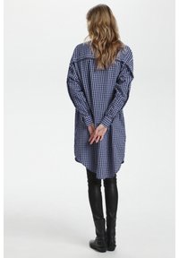 Blue and white checkered shirt dress with long sleeves, gathered shoulders, and a curved hem, paired with black leather leggings and ankle boots.