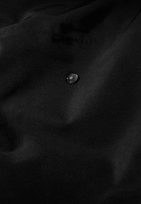 Schwarzer Stoff mit einer glatten, matten Oberfläche, auf dem ein einzelner Wassertropfen liegt, der die Wasserabweisung hervorhebt.