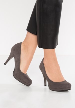 Décolleté grigie in suede con tacco alto, punta arrotondata, e soletta piatta, esposte accanto a pantaloni neri sartoriali.