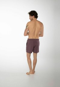 Costumi da bagno da uomo viola con vita elastica, tasche laterali e una texture liscia. Appaiono di lunghezza a metà coscia.