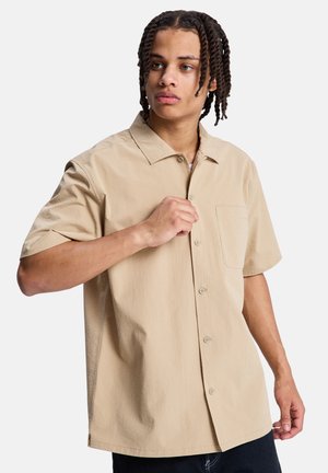 Chemise beige à manches courtes avec un tissu texturé, patte de boutonnage et une poche poitrine unique. Dotée d'un col ouvert et d'une coupe décontractée.