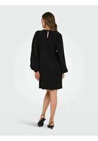 Black knee-length dress with vertical ribbed texture, puffed long sleeves, and a small back keyhole opening. Paired with black slingback heels.