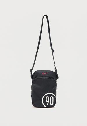 Fekete Nike oldaltáska állítható pánttal, piros Swoosh logóval fent, és fehér "90" nyomattal körben alul jobbra.
