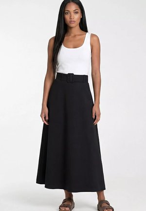 Kobieta stojąca, ubrana w biały top bez rękawów, czarną spódnicę o linii A z wysokim stanem i paskiem oraz brązowe sandały z odkrytymi palcami na jasnym jednolitym tle.