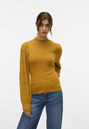 Haut jaune moutarde avec un corps ajusté et des manches longues texturées et bouffantes. Encolure ronde simple, associé à un jean large bleu.