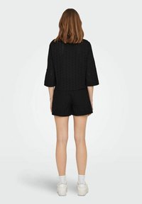 Completo a due pezzi nero composto da un top cortissimo con ritagli floreali e maniche ampie, abbinato a pantaloni corti coordinati. Indossato con sneakers bianche.