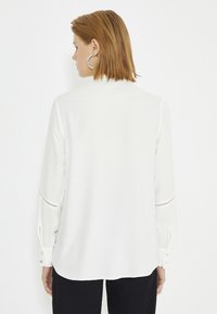 Witte blouse met lange mouwen, voorzien van knoopjes bij de manchetten en uitsparingen op de mouwen. Soepele stof, relaxte pasvorm, afgeronde zoom.