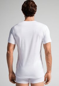 Witte T-shirt met korte mouwen, gemaakt van katoen, getailleerd ontwerp, gladde textuur, gedragen met bijpassende witte boxershorts, gezien vanaf de achterkant.