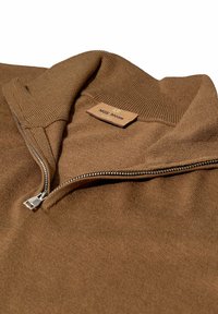 Hnedý pletený sveter s štvrťzipom, s rebrovaným golierom a strieborným zipsom, s viditeľnou značkou "MOS MOSH" na vnútornej strane výstrihu.