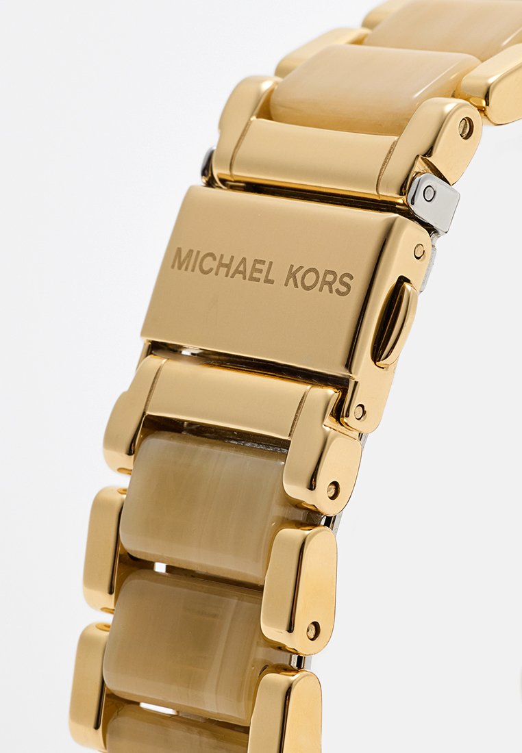 Montre en métal doré avec des maillons rectangulaires. Le bracelet présente des inserts lisses de couleur claire. Gravé "MICHAEL KORS" sur le fermoir.