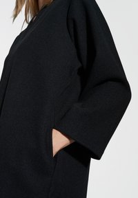 Zwarte kleding met een losse pasvorm, voorzien van driekwart mouwen, zijzakken en een gestructureerde stof.