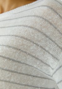 Weißer Strickpullover mit grauen horizontalen Streifen, der eine lockere Strickstruktur aufweist und durch kleine Pailletten einen dezenten Glanz erhält.