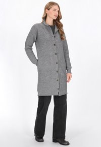 Szary sweter dzianinowy o ryflowanej fakturze i geometrycznym wzorze, z kołnierzem, zapinany na guziki, z bocznymi kieszeniami, zestawiony z czarnymi spodniami.