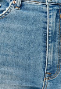 Jeans de mezclilla azul claro con el clásico diseño de cinco bolsillos, costuras visibles en naranja contrastante y un ligero desgaste en la cintura.