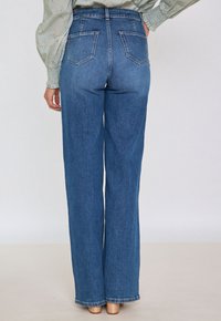 Jeans in denim azzurro chiaro a vita alta, con gamba dritta, dotati di due tasche posteriori e orlo pulito. Il materiale sembra essere testurizzato.