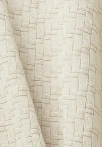 Tissu tricoté de couleur crème avec un motif tressé texturé et des plis doux.