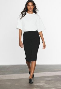 T-shirt blanc oversize avec des manches courtes et larges, associé à une jupe crayon noire à mi-genoux. Porté avec des chaussures noires à enfiler.