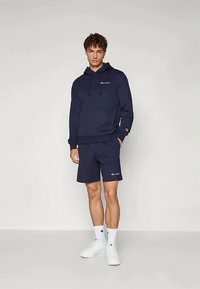 Hanorac navy cu pantaloni scurți asortați, confecționați dintr-un amestec de bumbac, având un logo pe piept și pe margine, cu manșete elastice și o croială relaxată.