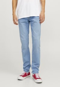 Jeans de mezclilla azul claro con corte recto, que presentan cinco bolsillos y una cremallera. Combinados con zapatillas rojas y una camiseta blanca.