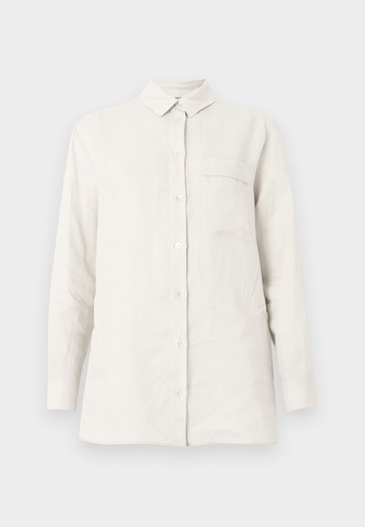 Λευκό πουκάμισο με μακριά μανίκια, κουμπιά, γιακά και μία τσέπη στο στήθος, εμφανίζεται σε απλό, ανοιχτό φόντο.