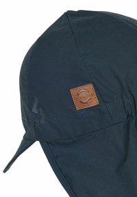 Mörkblå keps av mjukt, vattenavvisande tyg, med en läderpatch med logotyp och öronlappar för extra skydd. Synliga sömmdetaljer.