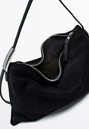 Zwarte suède handtas met een gebogen ontwerp, voorzien van een zilveren rits en een dunne schouderband. De binnenvoering is van donkere stof.