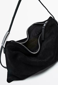 Black suede handbag with a curved design, featuring a silver zipper and a thin shoulder strap. The interior is lined in dark fabric.