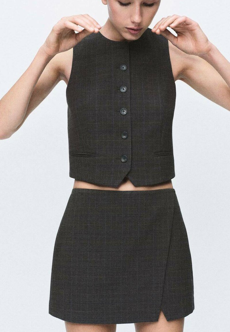 Conjunto de traje gris que incluye un chaleco recortado sin mangas con cierre de botones y una mini falda a juego con un detalle de abertura en la parte frontal.