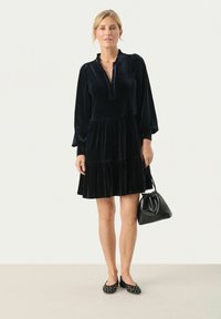 Robe en velours bleu marine avec une jupe à étages, des manches longues et un col à cran. Associée à un sac à main noir et des ballerines à pois.