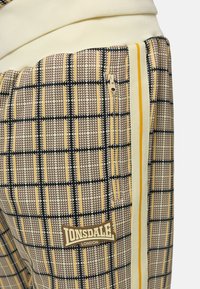 Lonsdale London mønstrede joggers i brunt, gult og creme, med en lynlås lomme, geometrisk design og kontrasterende sidelommer.