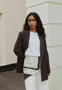 Brown blazer over a light blue top, paired with a patterned skirt in cream with black polka dots. White wide-leg pants complete the look.