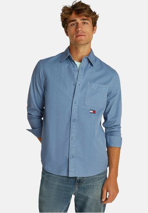 Camicia azzurra chiara con taschino sul petto, maniche arrotolate e una piccola toppa con logo. Realizzata in un morbido tessuto di cotone.