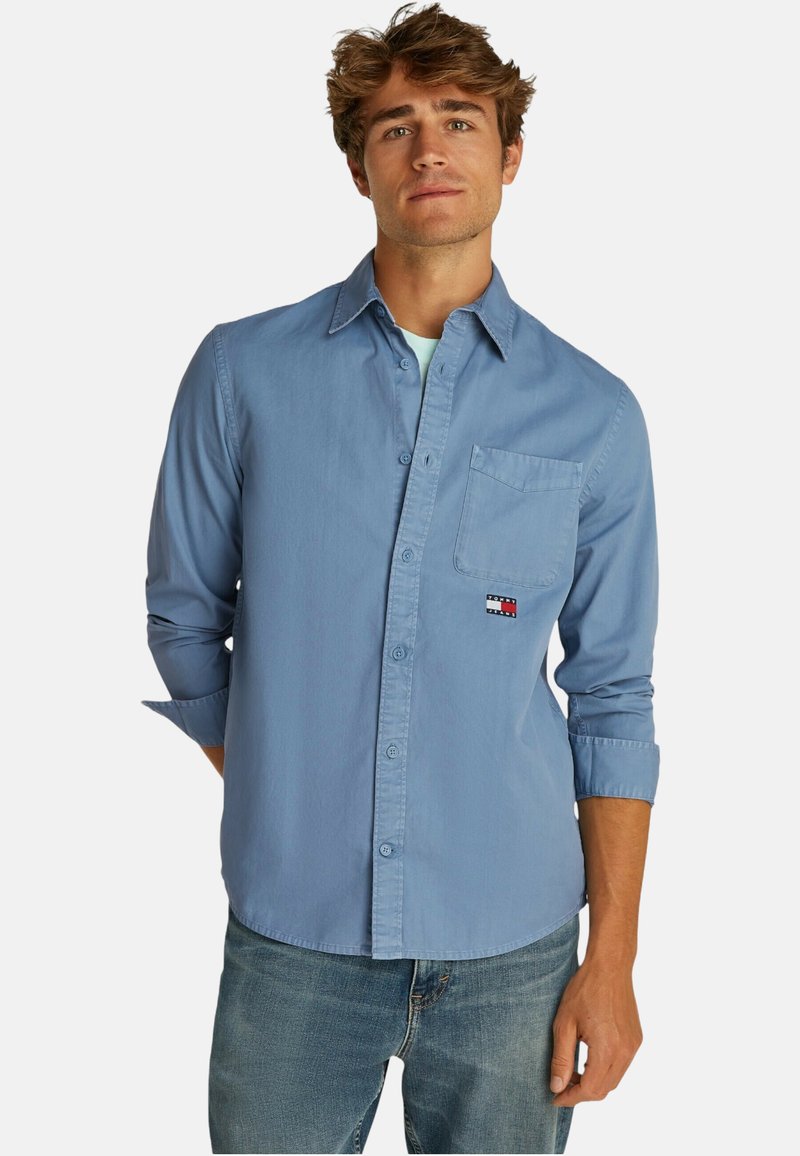 Camicia azzurra chiara con taschino sul petto, maniche arrotolate e una piccola toppa con logo. Realizzata in un morbido tessuto di cotone.