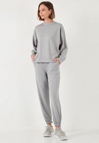 Hellgraues Sweatshirt und passende Jogginghose aus weichem Material; mit elastischen Bündchen, lockerer Passform und Seitentaschen. Weiße Sneaker runden das Outfit ab.
