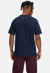 T-shirt en coton bleu marine avec un col rond, des manches courtes et une coupe décontractée, vue de dos, associée à un pantalon bordeaux.