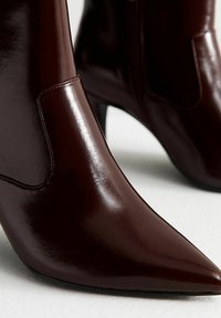 Burgundowe skórzane botki do kostki z ostrym noskiem i smukłym, wysokim obcasem. Gładka tekstura z bocznymi akcentami i elegancka sylwetka.