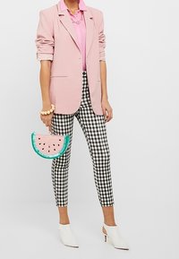 Blazer rosa, camicia rosa chiara, pantaloni a scacchi bianco e nero, mule bianche con tacco e una clutch a forma di cocomero rosa con accenti verdi.
