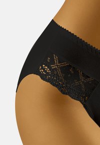 Zwarte kanten slip met een gestructureerde tailleband en ingewikkelde kantdetails aan de achterkant, in contrast met een gladde, matte afwerking.