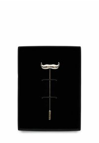 Silverfärgad slagmärke i form av en mustasch, monterad på en svart sammetbakgrund, med en elegant metallstam och en dekorativ ände.