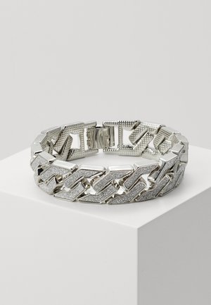 Silbernes Gliederarmband mit strukturierten und polierten Oberflächen, präsentiert auf einem weißen Podest vor einem hellgrauen Hintergrund.