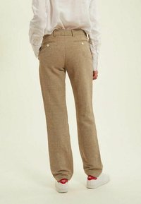 Pantalons à carreaux beige avec une coupe décontractée, dotés de deux poches arrière, d'une texture subtile et d'une ceinture lisse, associés à des baskets blanches.