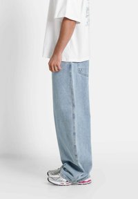 Luźne, jasnoniebieskie dżinsy o prostym kroju, w połączeniu z szaro-różowymi butami sportowymi oraz luźną białą koszulką.